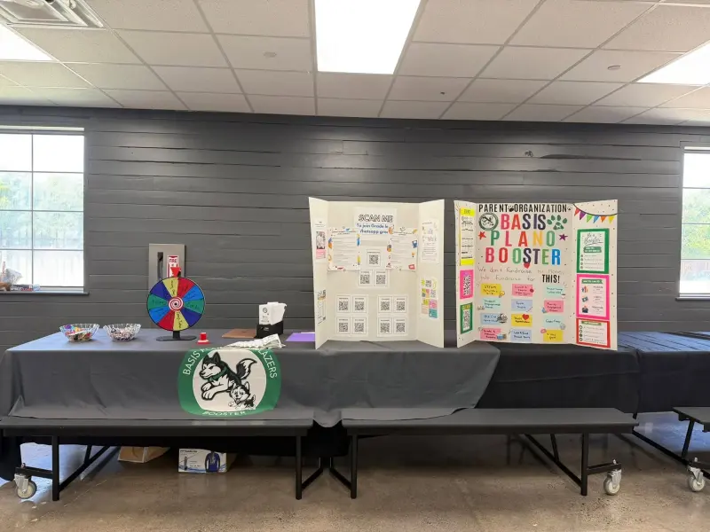 The Booster tables set up in the cafeteria before check-in, a spinning prize wheel at one end and two display boards behind