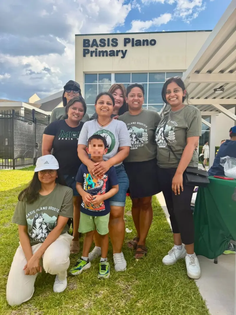 Volunteers and their children gathered for a group photo on the grass outside the BASIS Plano Primary entrance