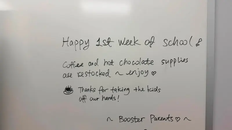 A whiteboard note from the Booster parents: happy first week of school, the coffee and hot chocolate supplies are restocked