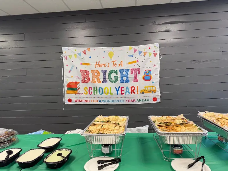 The buffet table below the bright-school-year banner, trays of quesadillas and tubs of sauces laid out on the green cloth