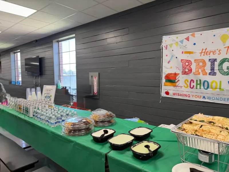 A long view of the drinks and dessert table running down the cafeteria wall, the banner at the far end