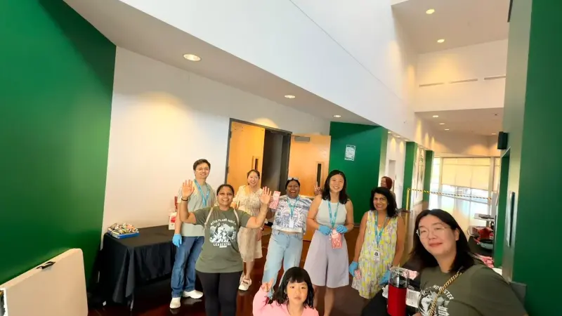 Booster volunteers in Leadership Team T-shirts waving from the popcorn table in the school lobby, striped popcorn boxes in hand