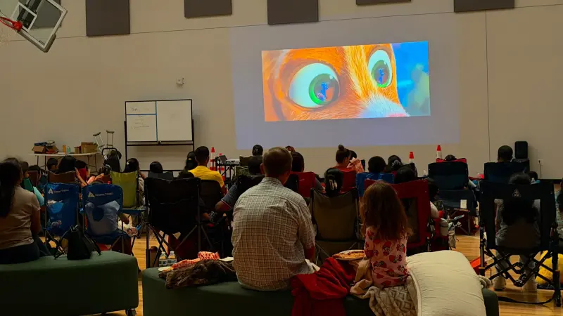 The audience seen from behind, silhouetted against a close-up of a wide-eyed animated character on the screen