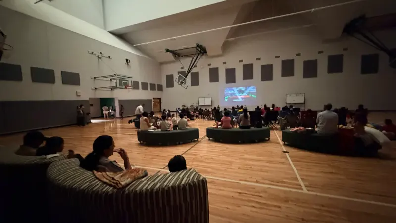 The gym with the lights down, families settled on benches and chairs around the glow of the screen