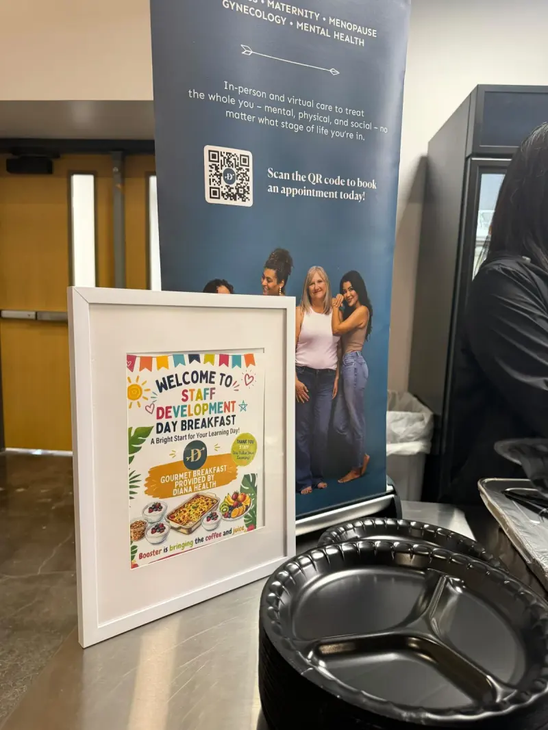 The framed welcome sign at the start of the serving table, a stack of black plates beside it and the Diana Health banner standing behind