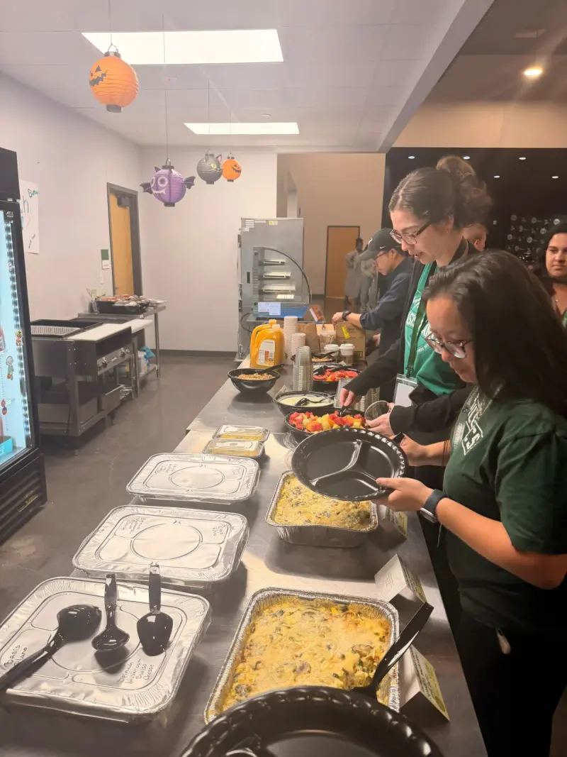 Staff in green school T-shirts filling their plates from trays of breakfast casserole and bowls of fruit