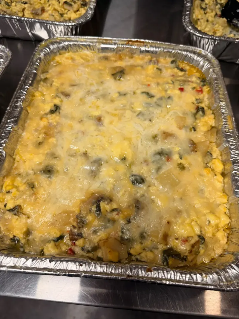 A foil tray of baked egg casserole with spinach, peppers and melted cheese