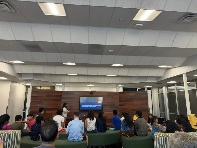 Families and students on green benches in the lounge, following a presenter through a “Myth or Truth?” slide about artificial intelligence