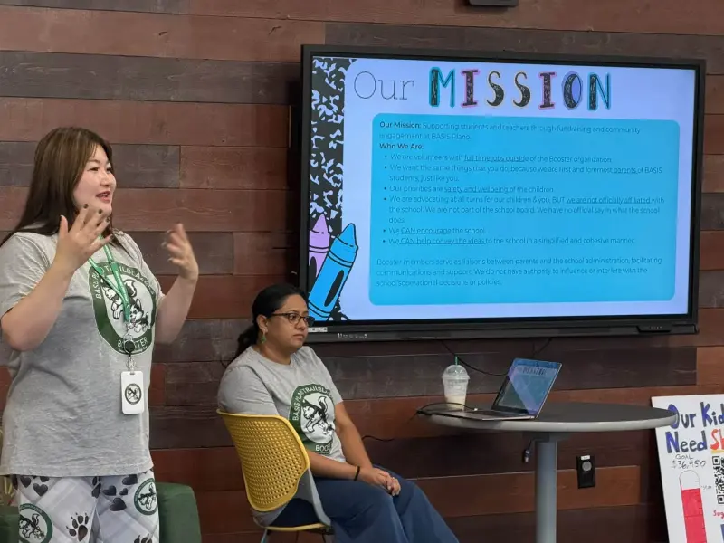 A Booster volunteer in a Trailblazers T-shirt talking through the “Our Mission” slide, another seated beside the laptop