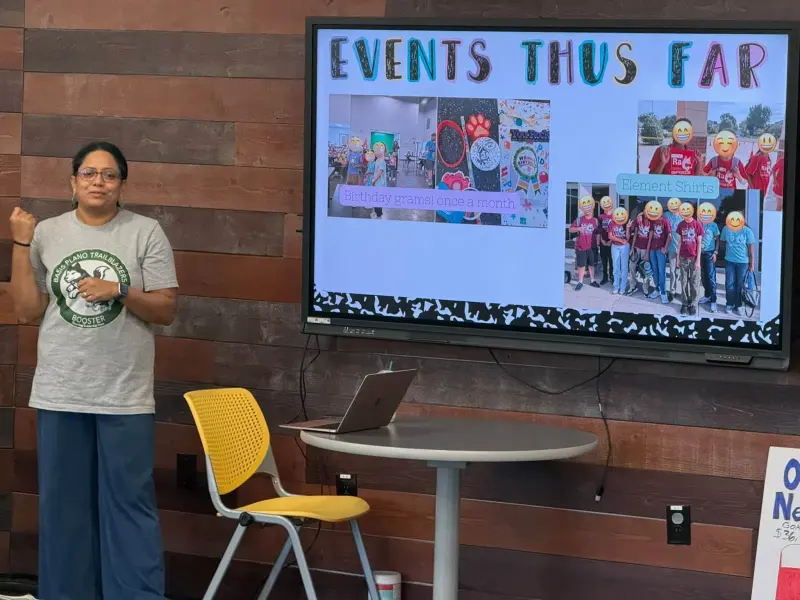 A Booster volunteer presenting an “Events Thus Far” slide showing Birthday Grams and Element Shirts, students’ faces covered with emoji
