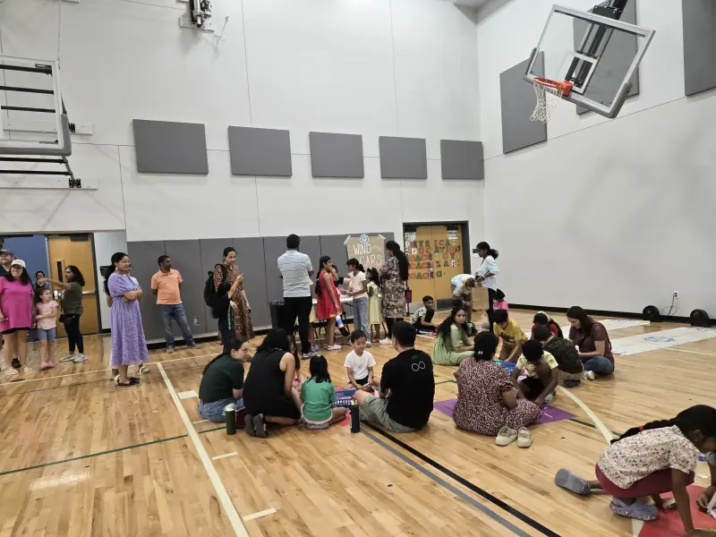 Children and parents gathered round baskets of craft supplies on the gym floor while families queue at the “Wind Cars” station table beneath a basketball hoop