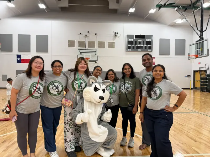 Booster volunteers in grey Trailblazers Booster T-shirts lined up on the gym floor, Blaze the Husky mascot kneeling in front of them