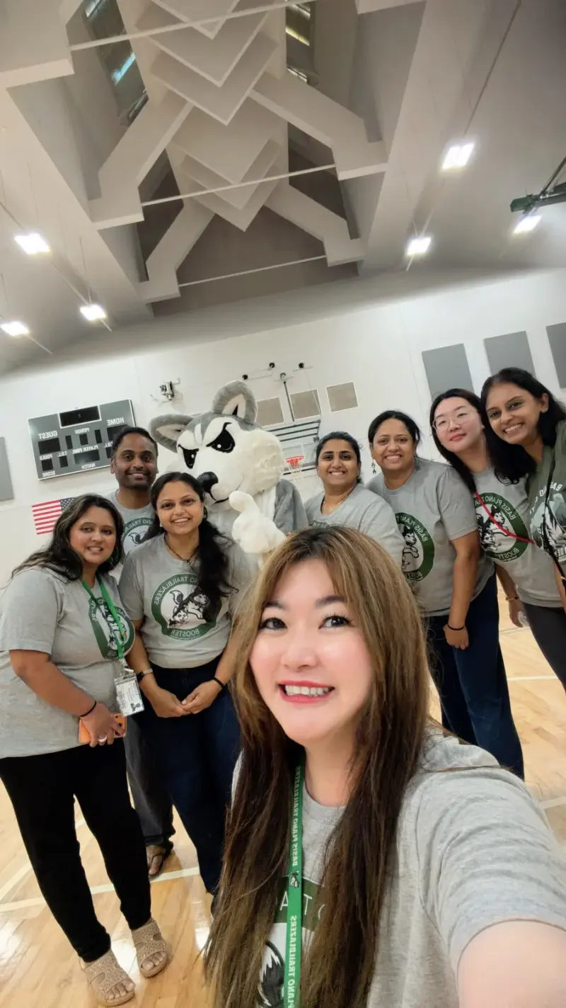 A selfie of the Booster volunteers crowded round Blaze the Husky mascot, the gym’s criss-cross ceiling beams overhead