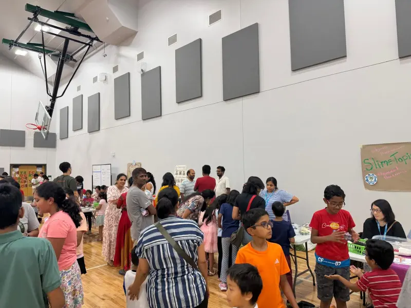 The Main Gym busy with families moving between activity tables, the hand-lettered “SlimeTopia — Chemical Reactions” sign on the wall