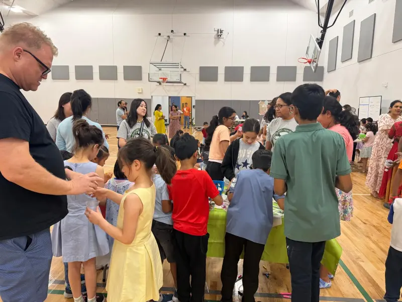 Children crowding round a green-covered activity table with clear plastic cups in hand, Booster volunteers in Trailblazers T-shirts helping from the far side