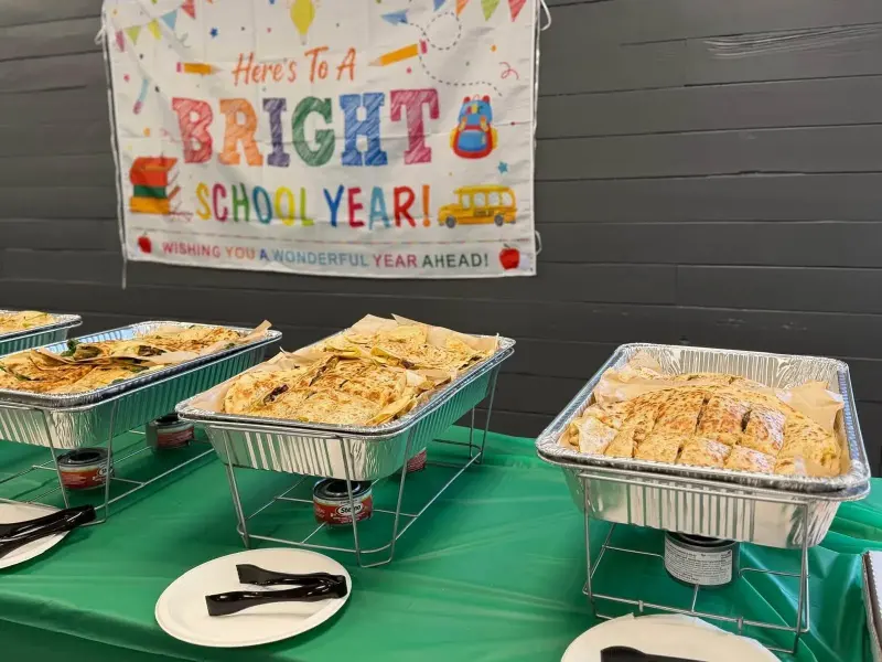 Three foil trays of quesadillas over their warmers, the bright-school-year banner on the wall above