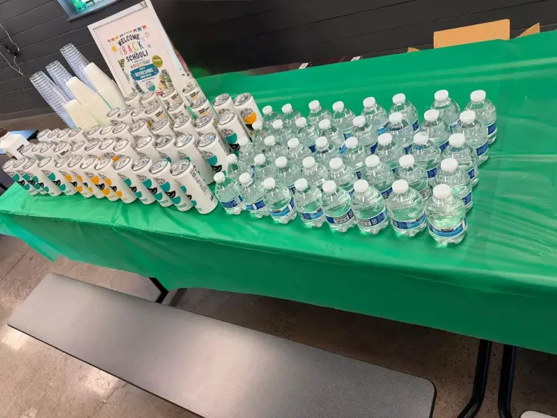 Cans and small water bottles arranged in blocks across the green cloth, cups and the welcome sign at the far end