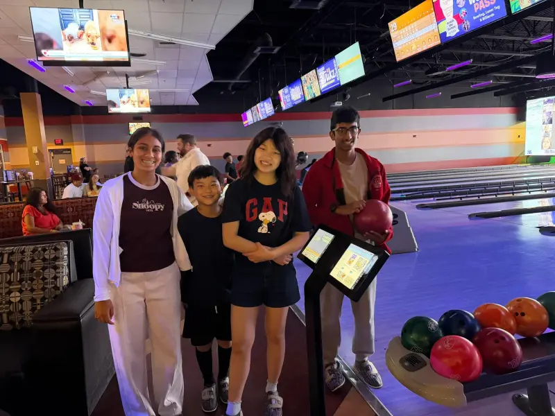 Four students posing at the end of a bowling lane, one holding a red ball, the rack of coloured balls beside them