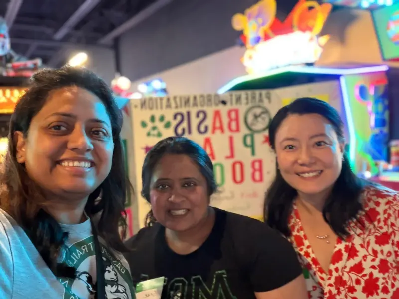 A close selfie of three volunteers in Booster shirts in front of the display board