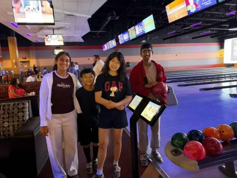 Four students at the end of a bowling lane, one holding a red ball, the ball return beside them