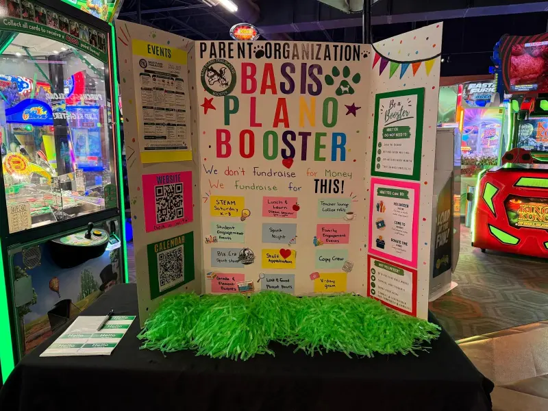 The Booster display board set up on a black table at the arcade, green pom-poms bunched along the front