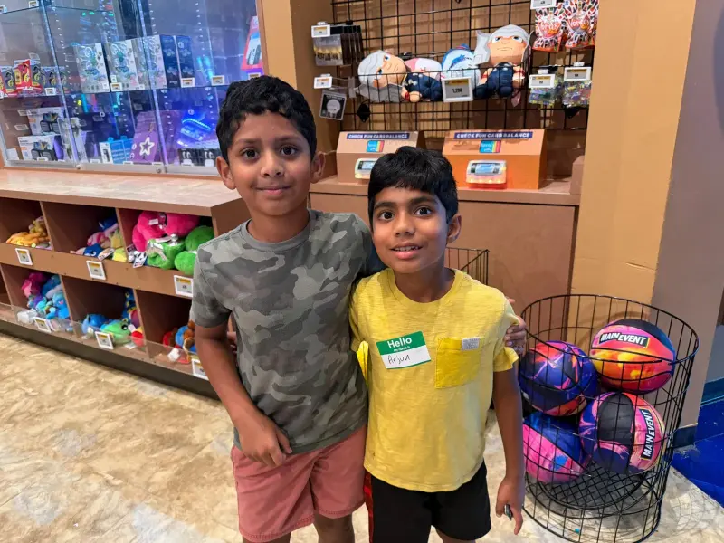 Two boys with an arm round each other’s shoulders at the prize counter, shelves of plush toys behind them