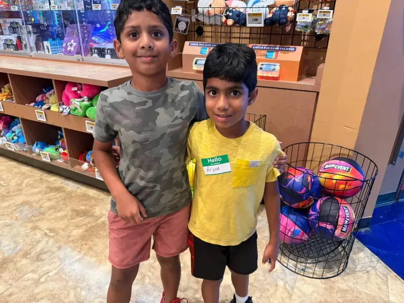Two boys standing side by side at the prize counter next to a wire basket of arcade basketballs