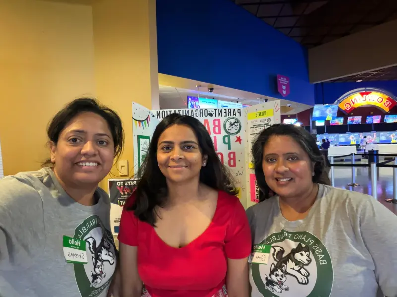 Three volunteers in Booster shirts and name stickers at the bowling desk, lanes and neon sign behind