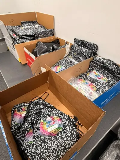 Boxes of goodie bags packed and ready: drawstring bags printed like a black-and-white composition notebook, each with a rainbow “Composition Book” label
