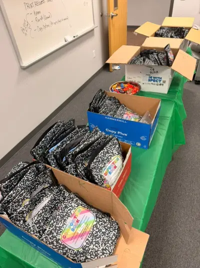 The handout table under a green cloth, a row of boxes filled with composition-notebook goodie bags and a tin of wrapped sweets at the far end