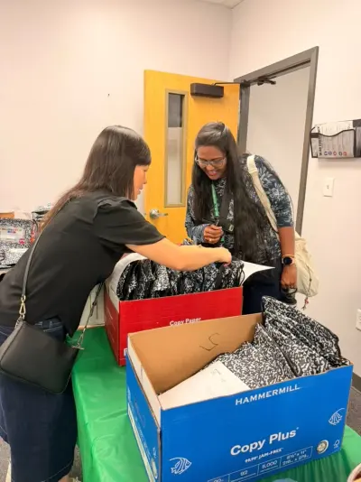 A volunteer reaching into a box of goodie bags for a smiling staff member at the handout table