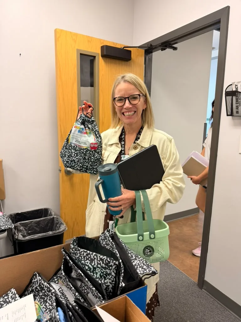 A smiling BASIS Plano teacher holding up a World Teacher Day goodie bag from the Booster